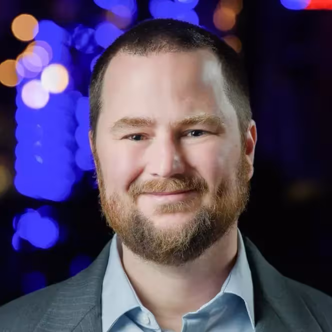 Headshot of Mike Herchel smiling in suit with a blue background