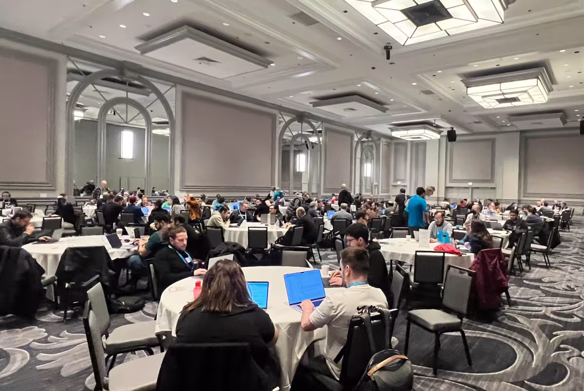 Large group of people around tables in a hotel ballroom with computers
